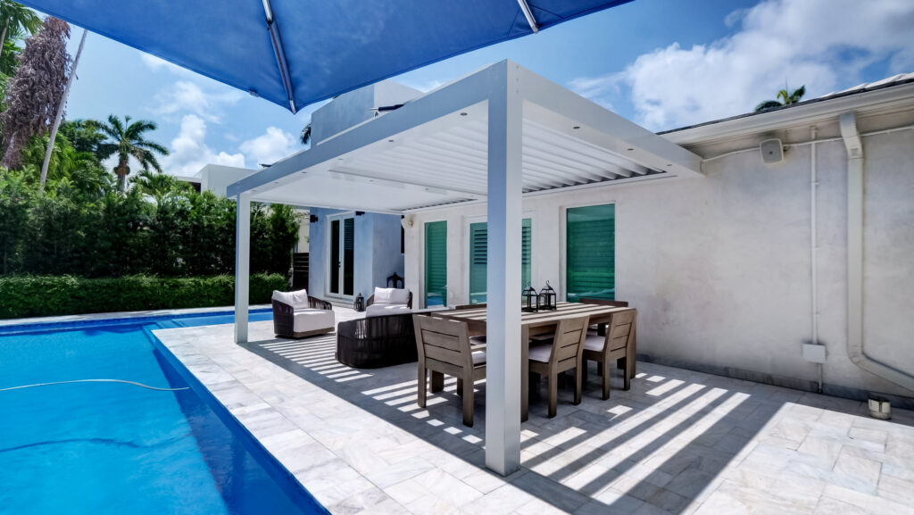 picture of white sundance louvered pergola with white louvers and perimeter lighting mounted to a home next to pool front view