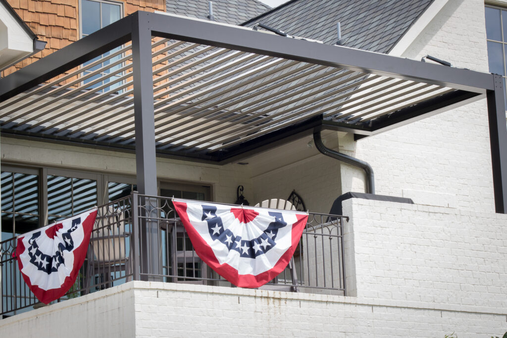 picture of bronze louvered pergola with tan louvers mounted to home and bronze gutter attached