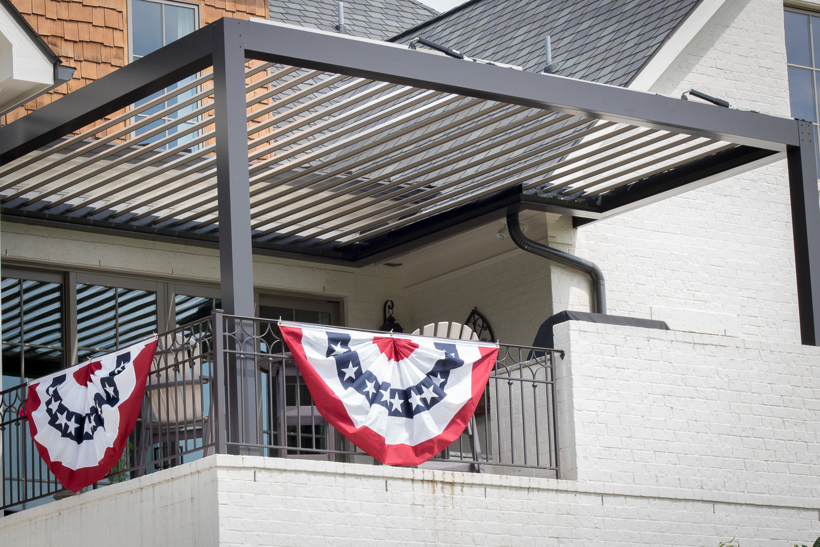 Bronze Sundance louvered pergola with tan louvers mounted to a home with a bronze gutter