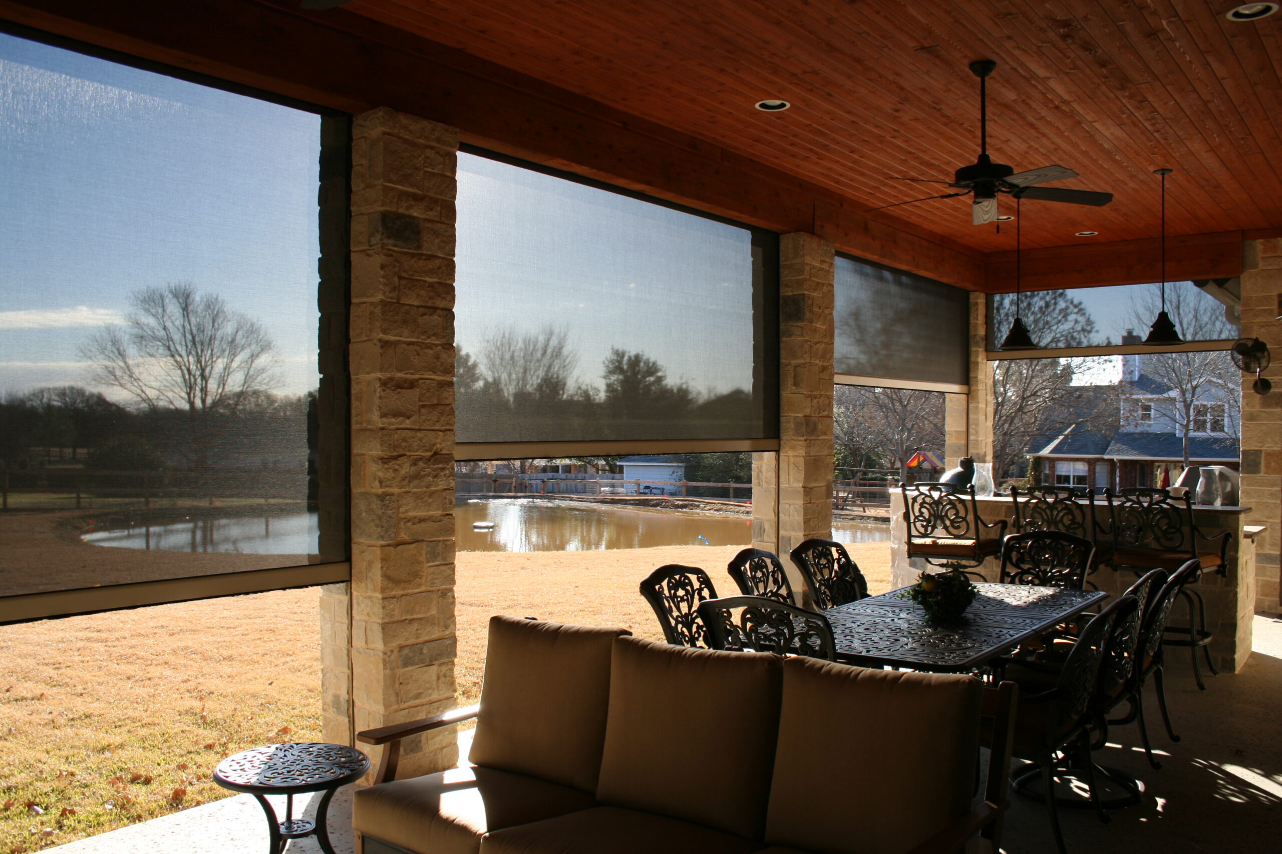 Rainier powered screens in dark gray fabric lowered around a covered patio with a dining table and seating