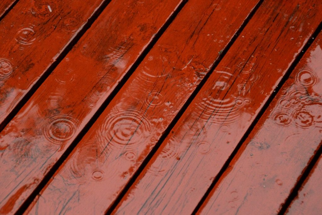 Raindrops creating ripples on a wet red wooden deck
